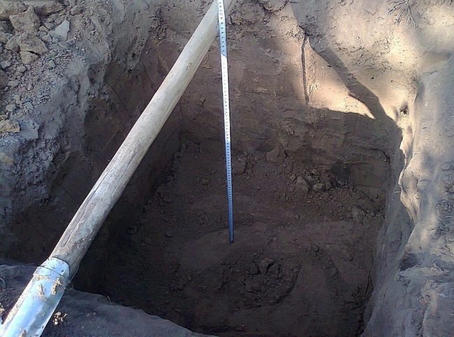 Посадочная яма для саженца винограда, черенок лопаты и рулетка для замера глубины