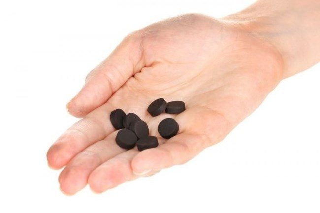 Несколько черных таблеток активированного угля в руке садовода