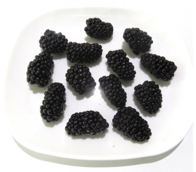 Черные перезрелые плоды ежевики удлиненной формы в белой тарелке